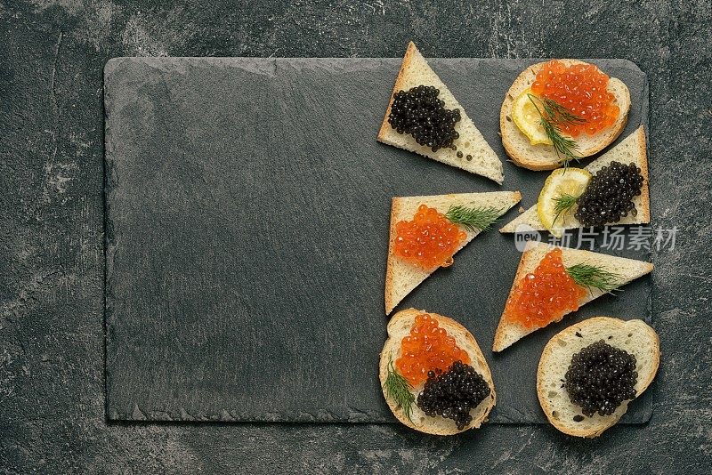 三明治与红鲑鱼和黑鲟鱼子酱在一个黑色的石头板在黑色的桌子上，顶视图与拷贝空间。