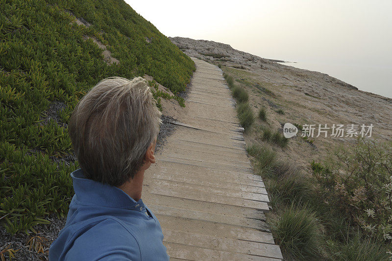 一个男人站在海边的木板路上