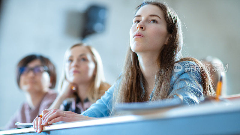 美丽的年轻女孩在教室里听讲座。多元种族的学生在大学学习。