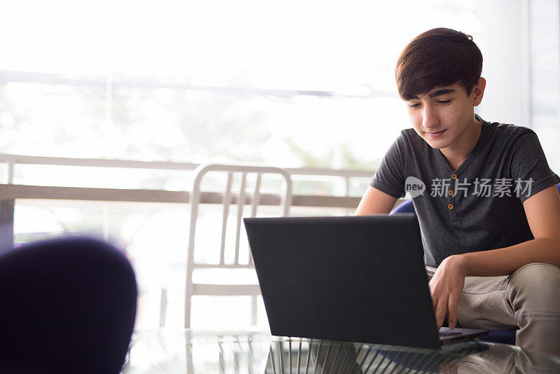 年轻英俊的伊朗少年在家里休息时使用笔记本电脑的肖像
