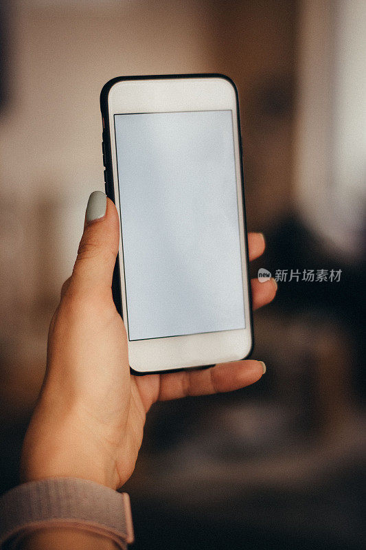 女士的手握现代白色智能手机与白色空屏幕