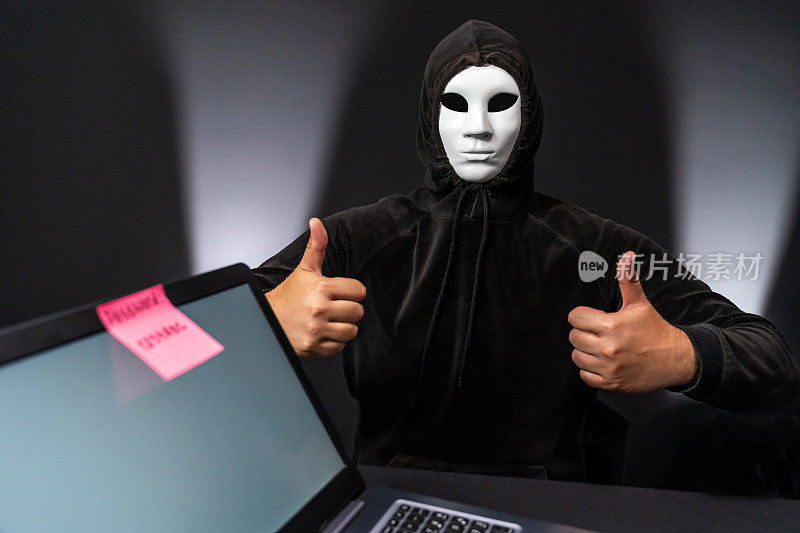 戴面具的电脑黑客竖起大拇指。笔记本电脑屏幕上的弱密码提示。
