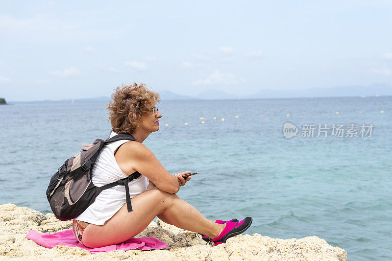 坐在海滩上玩智能手机的资深女性