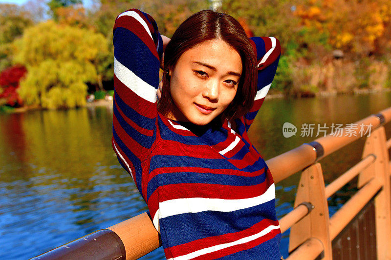年轻的日本女子站在桥上，对着美丽的秋叶，在井岛公园，东京