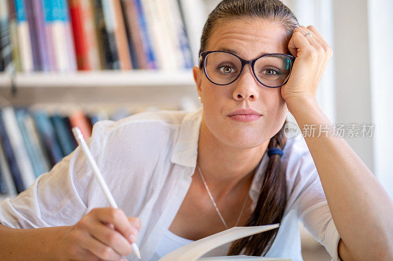 疲惫的女学生坐在图书馆桌子旁的肖像