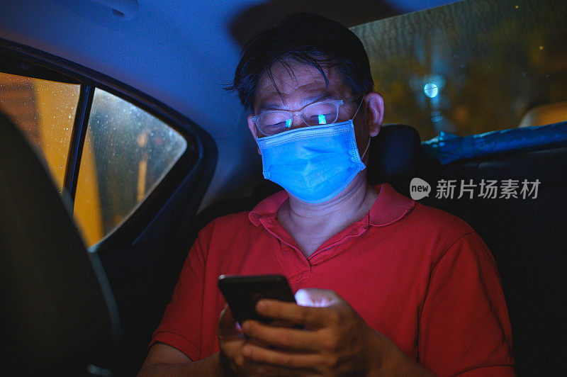 亚洲男性乘客在出租车内使用智能手机时戴上口罩
