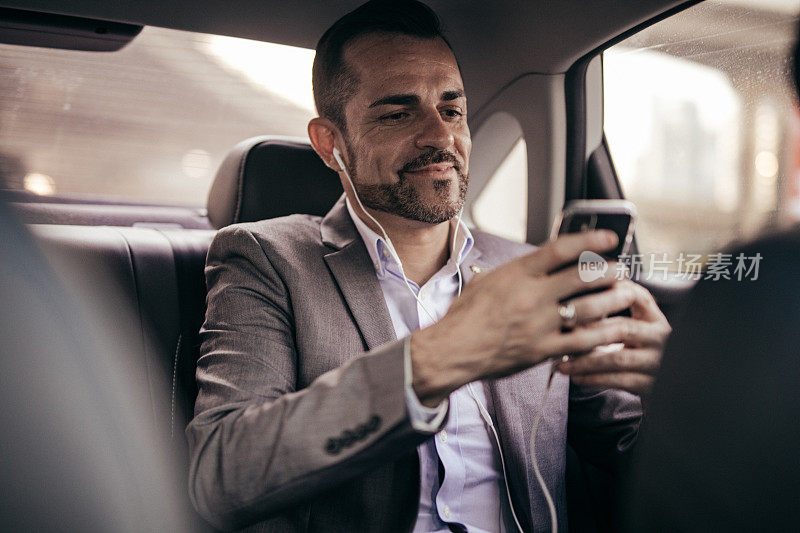 现代人坐在汽车后座上，用着智能手机