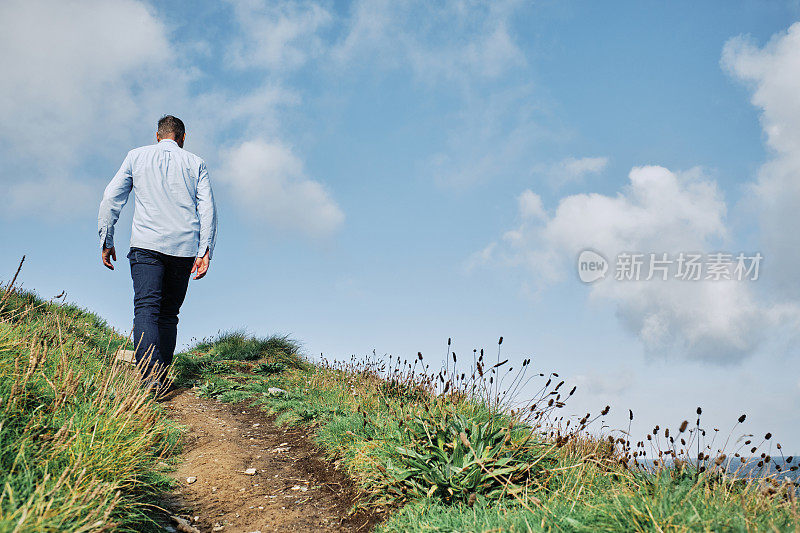 一个阳光明媚的秋日，康沃尔郡纽基市Pentire的男子走在西南海岸的人行道上。