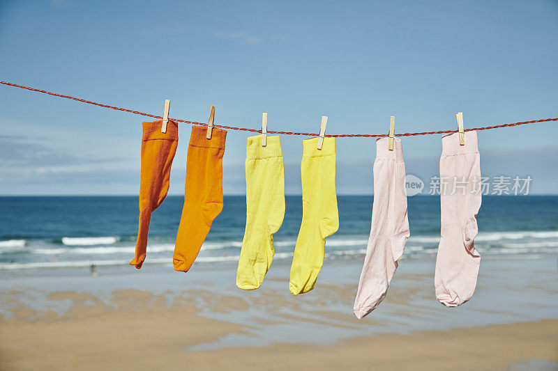 三双色彩鲜艳的袜子挂在晾衣绳上，俯瞰着阳光明媚的海滩。