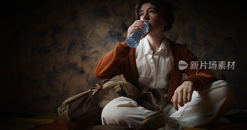 女人坐在背包旁边喝着水