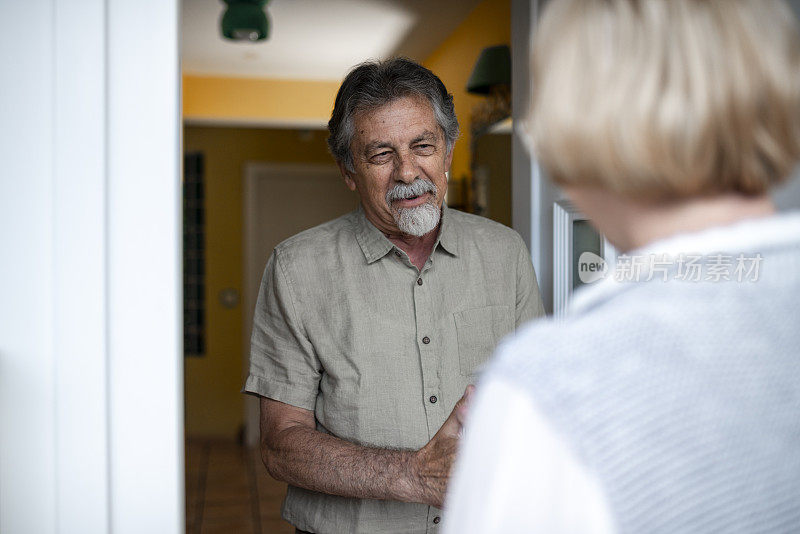 一名老年男子打开前门，迎接一名女性保健工作者进行家庭健康访问
