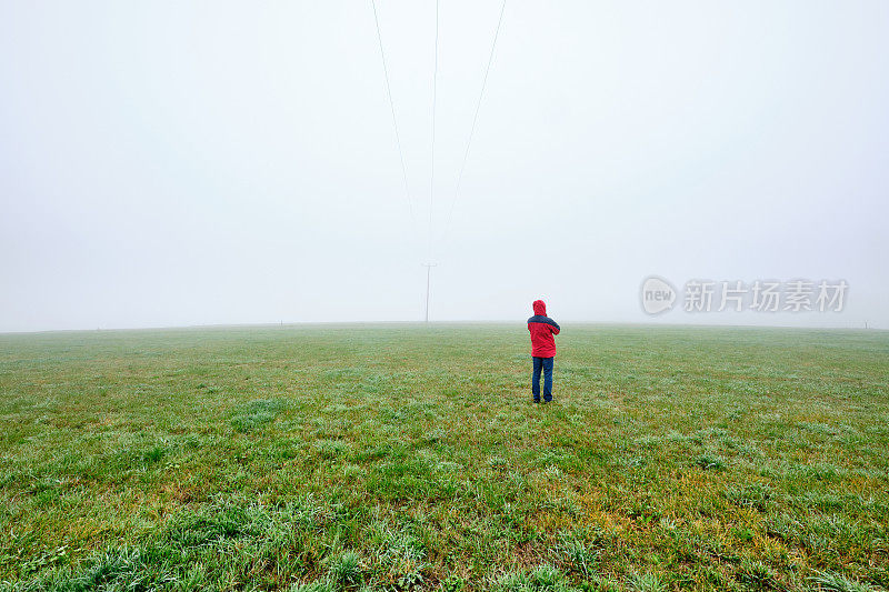 在浓雾中，身穿红色夹克的人站在草地上的背影