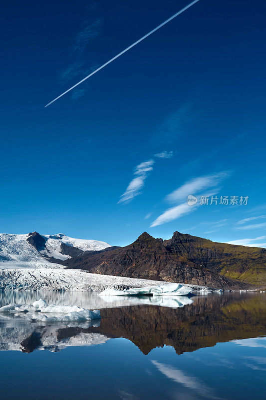 令人惊叹的风景，清澈的湖泊和冰块反射山脉在明亮的蓝色天空和飞机轨道。Jokulsarlon、冰岛
