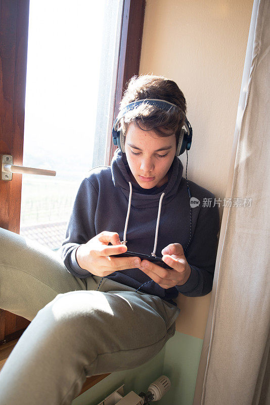 十几岁的男孩戴着耳机玩智能手机游戏