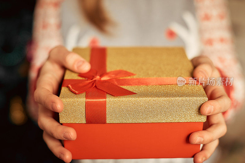 圣诞礼物，一个女孩的手拿着一个金色的礼盒在圣诞树的背景下，新年的概念