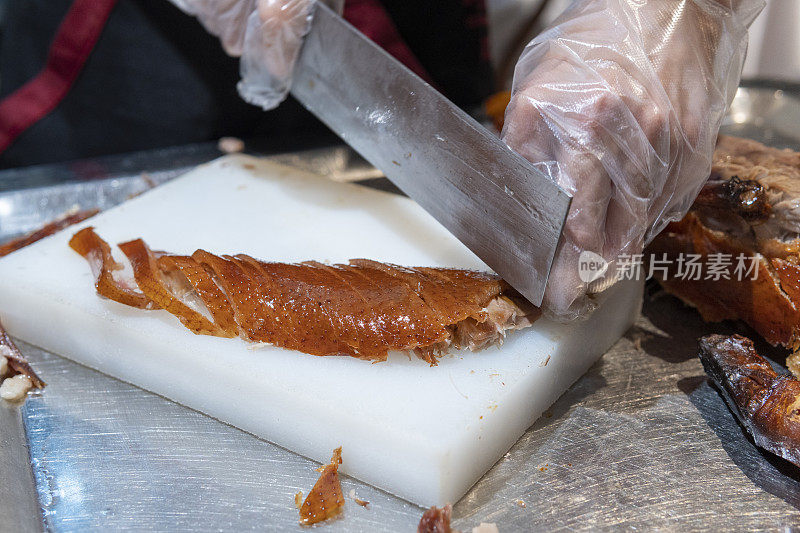 一位厨师在一家餐馆的厨房里切着美味的北京烤鸭