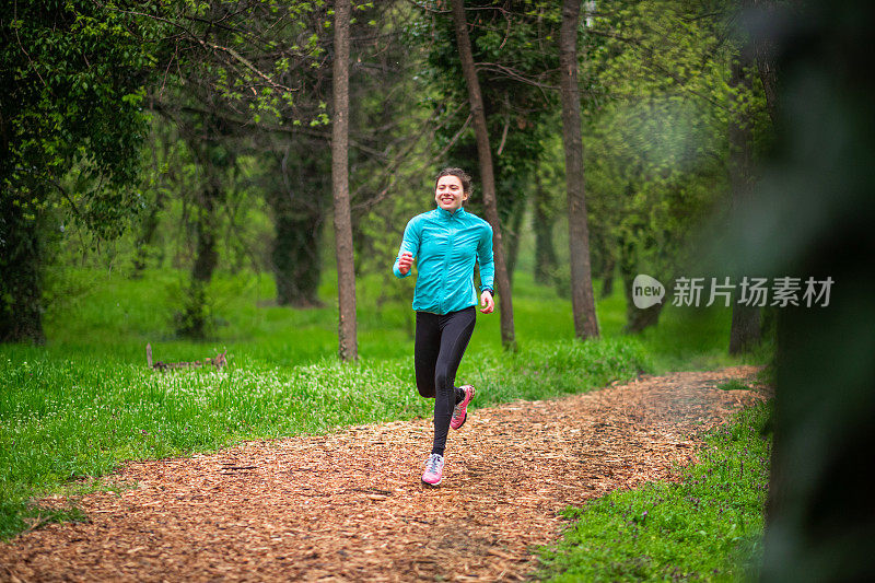 微笑少女慢跑在覆盖跑道上的树林