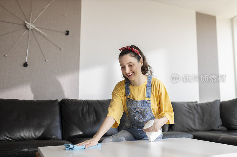 快乐的年轻女人用喷雾剂和抹布打扫房间