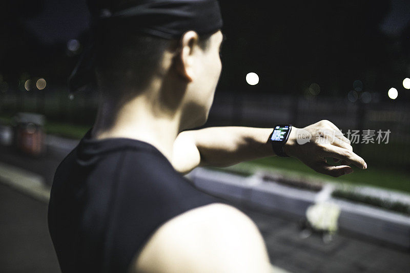 年轻人在夜间跑步时用智能手表查看心率