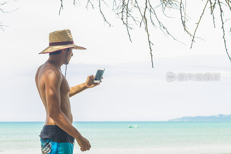 在拉丁美洲的海滩上，一位健康的拉丁男子在等待冲浪时用手机发短信。