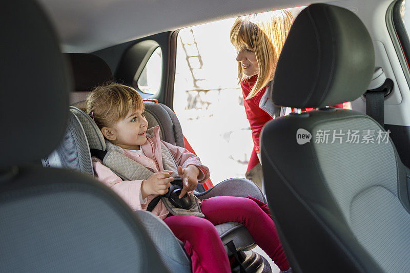 一位女士正在检查她女儿坐在汽车座椅上的情况