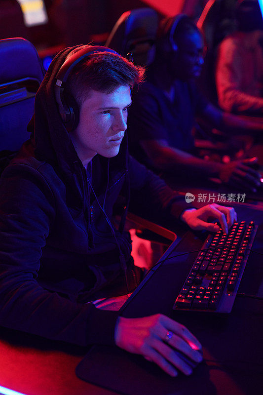 严肃的年轻电竞玩家穿着连帽衫戴着耳机在准备比赛的时候玩在线游戏