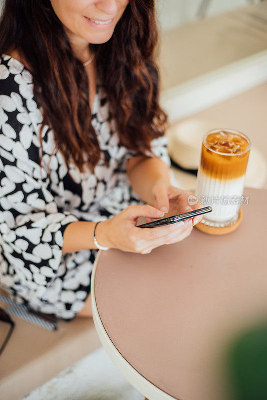 一个女人用手机和朋友发短信，在咖啡馆喝咖啡