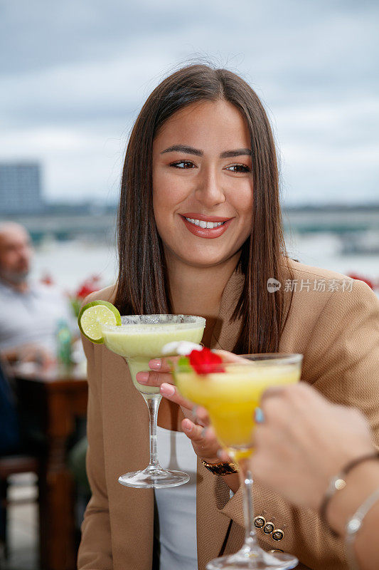 年轻女子微笑着和朋友在室外餐厅的餐桌上敬酒