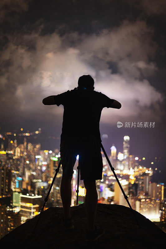 香港，一名男子站在相机和三脚架上拍摄夜景