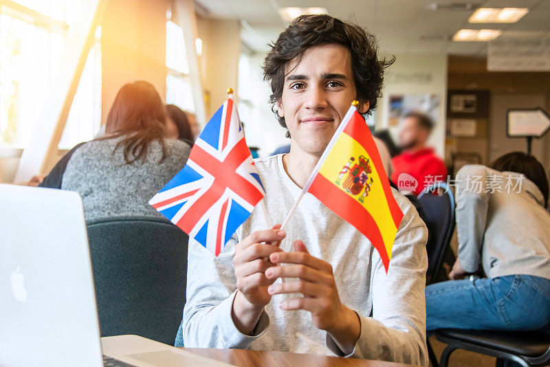 奉献的男大学交换生，在他的大学图书馆里举着一面西班牙国旗和一面英国国旗