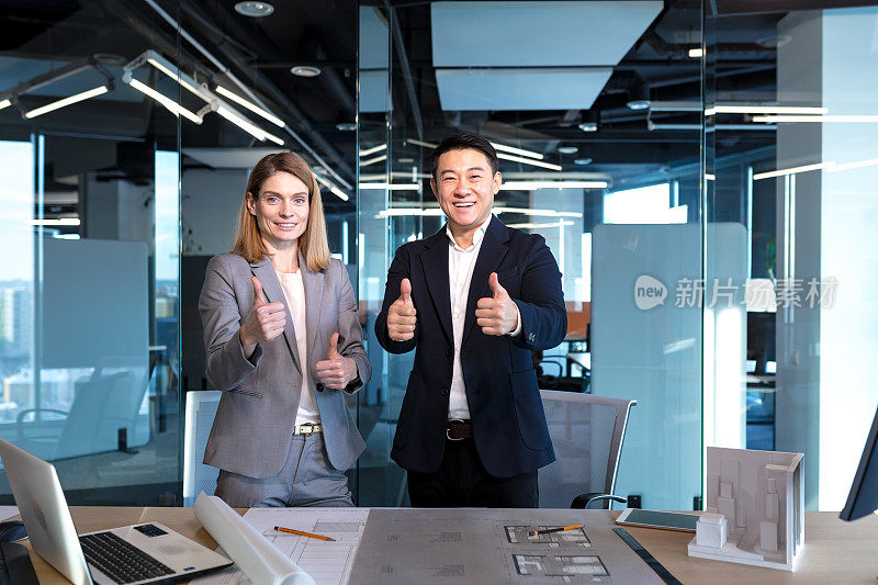 一群成功的建筑师，一名亚洲男性和一名女性，为项目的成功完成而欣喜，看着相机，竖起大拇指，开心地微笑着，为商业伙伴而欣喜