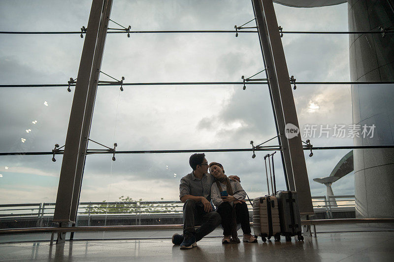 一对亚洲华人夫妇坐在机场窗前等待登机