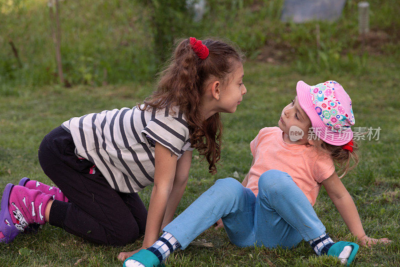两个小女孩坐在草地上，互相望着对方