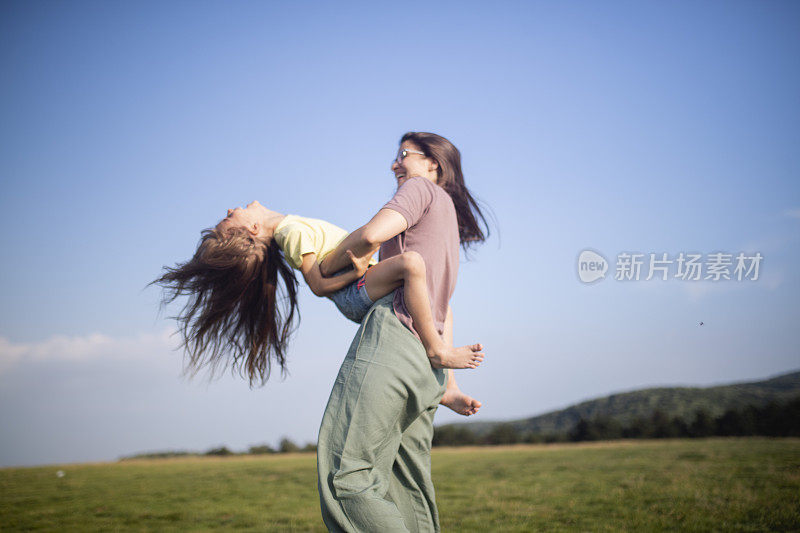 一个微笑的女人和她的女儿在大自然中玩耍。