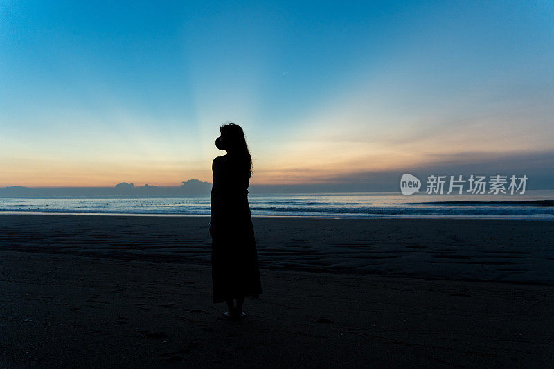 年轻的亚洲女子站在海边看日出