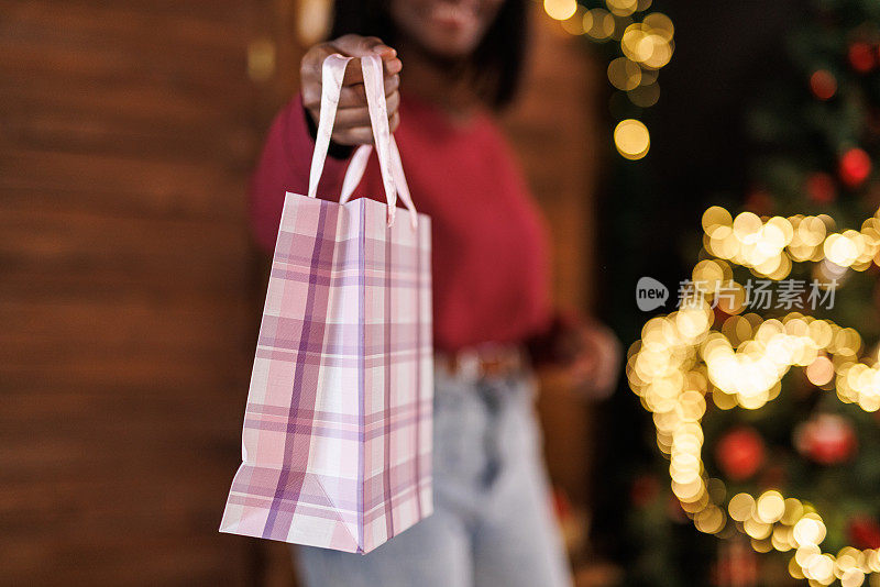 一名年轻女子走到一棵圣诞树前，手里拿着很多礼物袋