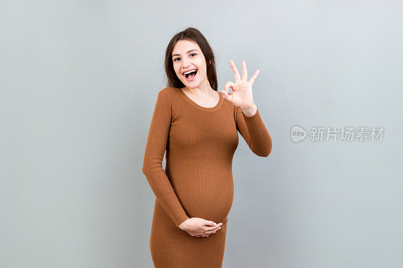 积极的孕妇显示对她的腹部在彩色背景好的手势。轻松愉快的怀孕。本空间