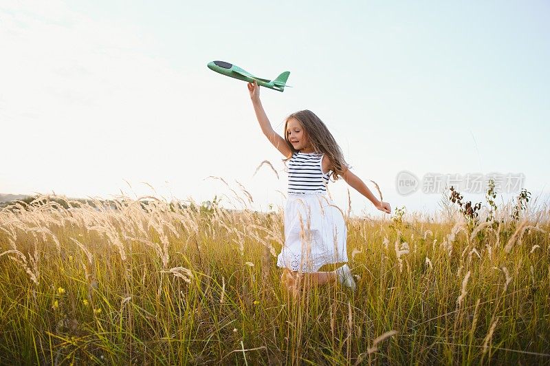 在落日的余晖中，快乐的女孩带着玩具飞机在田野上奔跑。孩子们玩玩具飞机。少年梦想着飞行，成为一名飞行员。女孩想成为一名飞行员和宇航员。缓慢的运动。