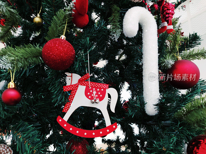有装饰品、圣诞球和玩具的圣诞树。红白相间的挂饰。漂亮的球，明亮的浆果和球果。雪糖棒。玩具-摇摆马