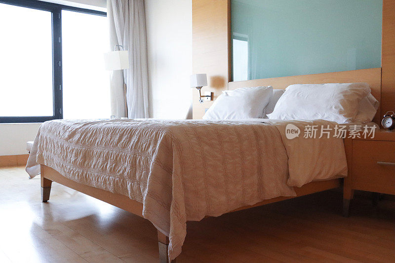 双人床的组合，木质和玻璃的床头板，白色的枕头，折叠的羽绒被，床头柜上的复古闹钟，壁挂式电灯，聚焦于前景