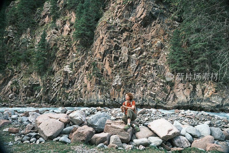 开朗的成熟女游客正在拍摄她在山河岸边徒步旅行的视频