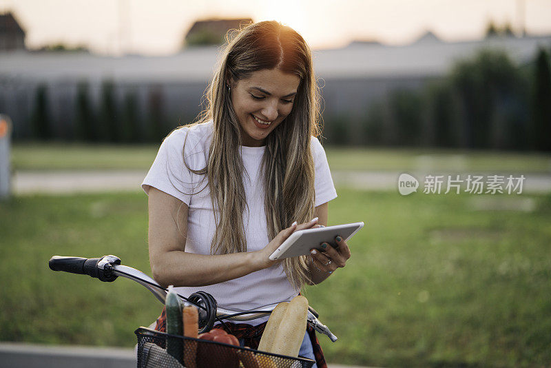 漂亮的年轻女子坐在自行车上，手里拿着平板电脑