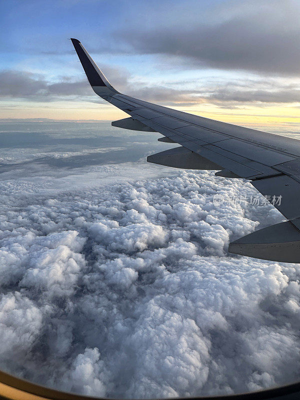 从飞机窗口看到的图像，飞机机翼在云层之上，蓬松的白云在海上，小翼和板条，橙色的日落，重点在前景