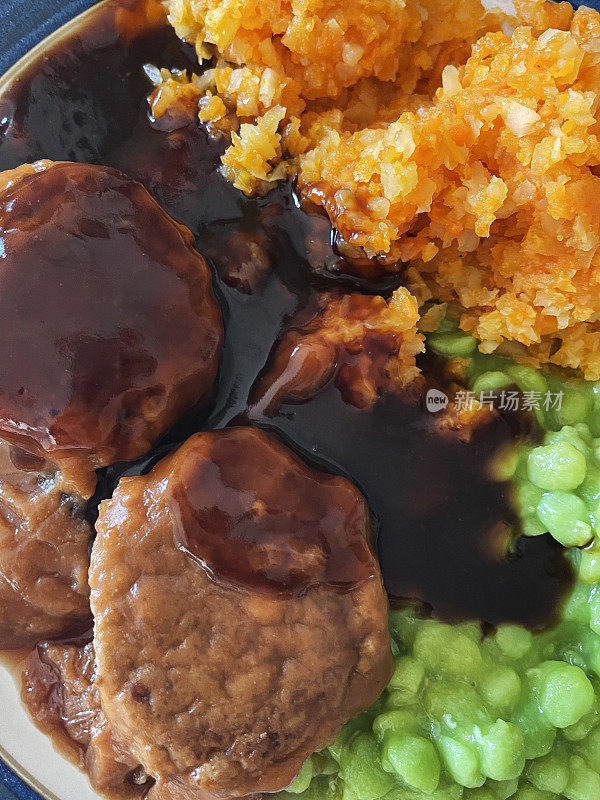 全画幅的图片，肉丸(内脏)，糊状豌豆，胡萝卜泥和肉汁餐在一个蓝色边缘的盘子，抬高视图