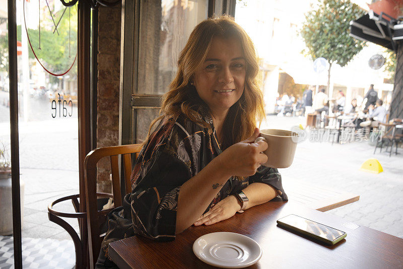 快乐的年轻女子在咖啡馆用手机喝咖啡