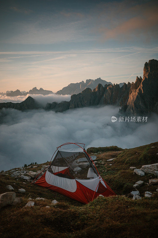 在白云之上的山顶上搭帐篷。在日落时分徒步旅行到未知的地方