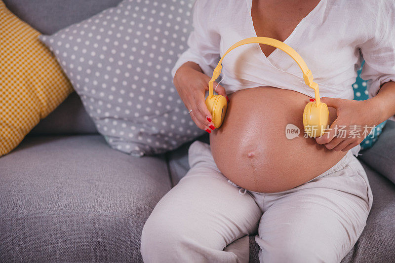 怀孕的年轻女子把耳机戴在肚子上