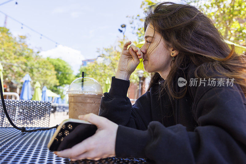 在街边咖啡馆喝冷饮休息一下。年轻的黑发白人女人抓鼻子，在街边咖啡馆喝奶昔。汉普顿步行在市中心区，弗吉尼亚州