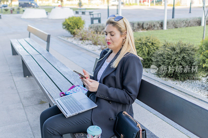 女人一边使用科技，一边享受城市的绿色空间。在户外灵活工作。现代虚拟理财咨询。
