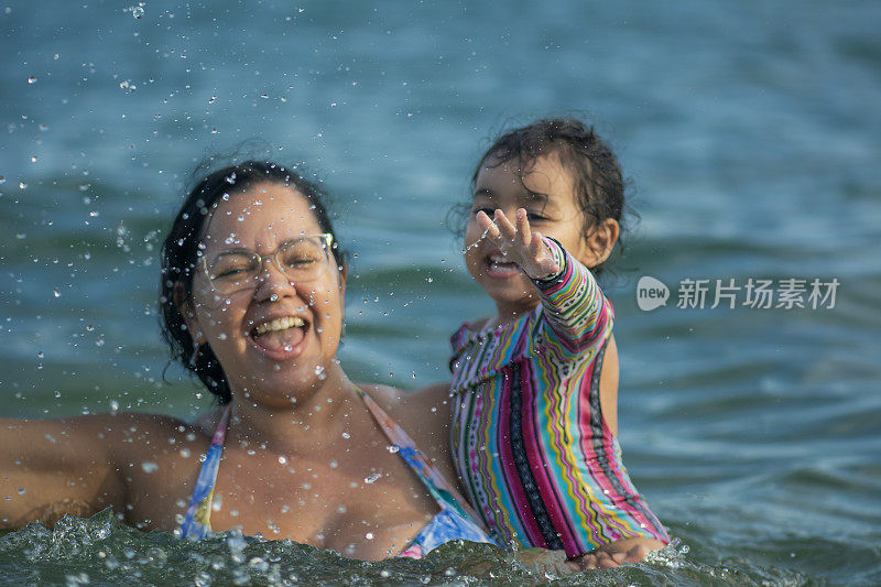 慈爱的妈妈带着女儿在海里戏水。水滴。